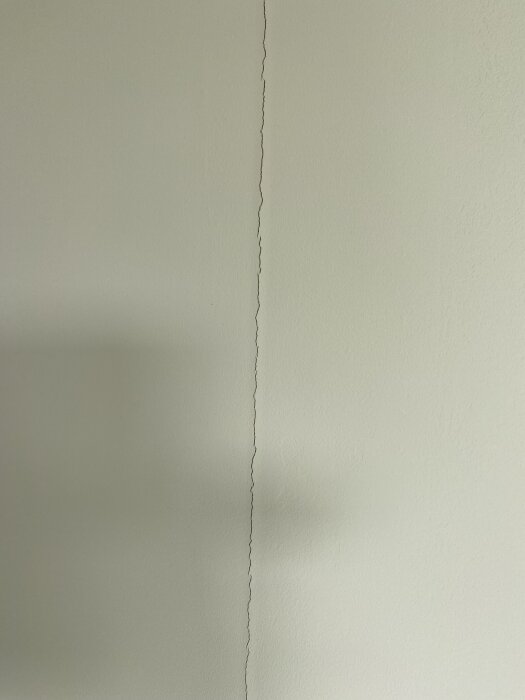 Spricka i en gipsskarv på en vitmålad vägg i en friggebod, ett problem som kan bero på användning av fel typ av skarvremsa.