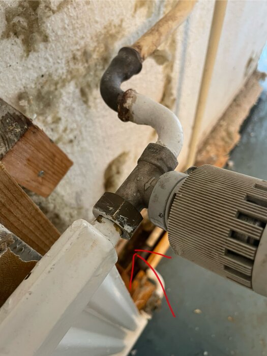 Värmerör med koppling och ventil vid radiator i källare, röd pil markerar specifik del av kopplingen.