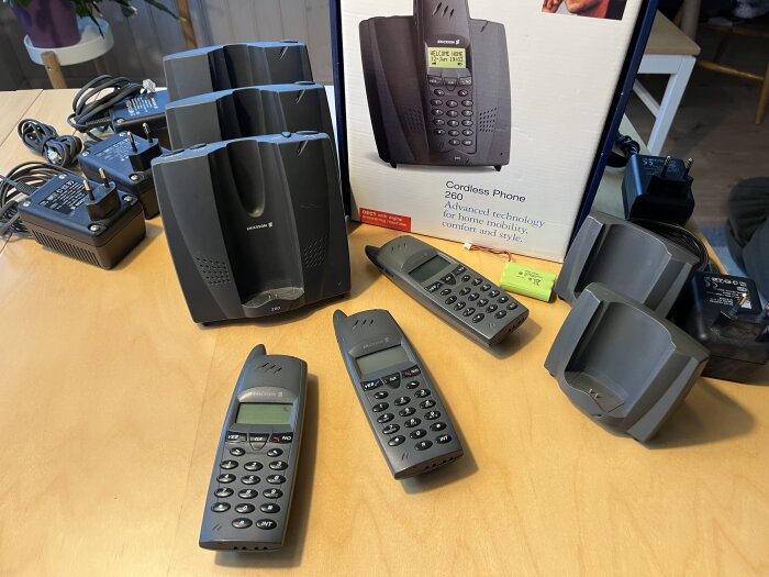 Gammalt Ericsson trådlöst telefonsystem med tre telefoner, basstationer, laddstationer och förpackning på ett bord.