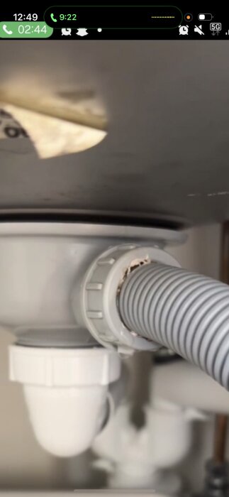 En närbild av en grå slang och koppling under en köksvask där det har läckt vatten.