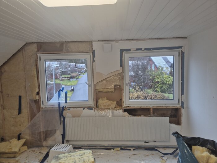 Öppen vägg och synliga reglar ovanför och under två fönster, med isolering och fuktskador, samt ett element i mitten av bilden.