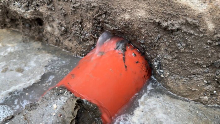 Orange avloppsrör vid husvägg med tydligt läckage av vatten och tecken på erosion runt röret.