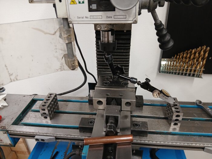 Fräsmaskin i ett garage med metallblock och justeringsverktyg på arbetsbordet, omgiven av borrverktyg och skyddspanel.