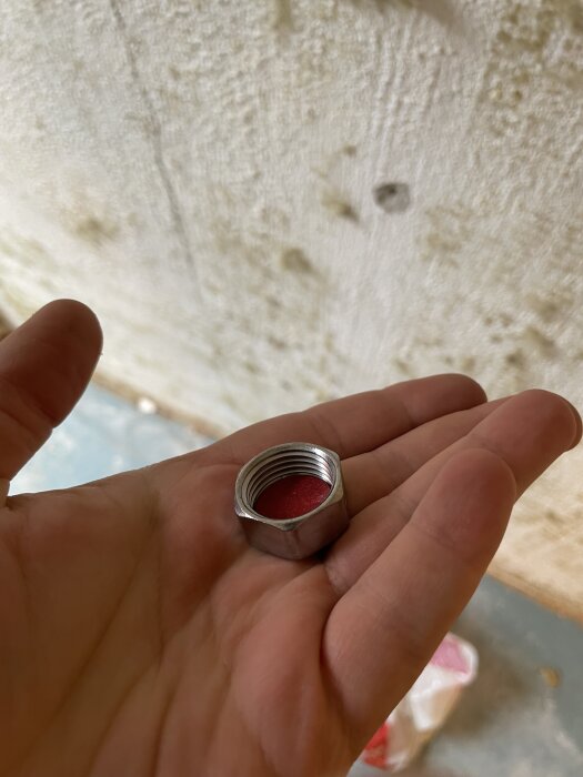 Person håller en metallmutter i handen, lutar mot en vägg, med en röd insida.