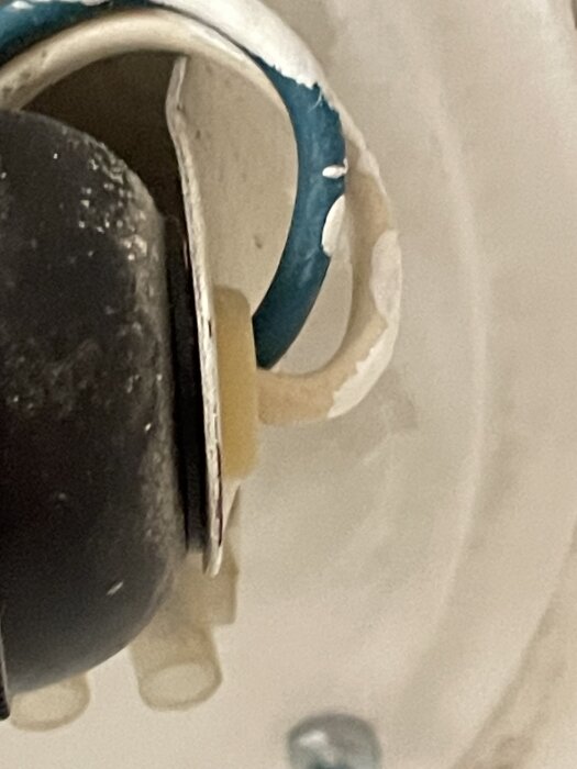 Närbild på en skadad gummiring i en taklampa, vilket gör att ljuskällans klot hänger ner mot glaskupan.