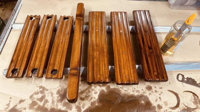 Behandlade teakdetaljer till båt ligger på ett bord för torkning. En pensel står i en burk med lacknafta bredvid.