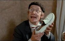 Okänd person i glasögon och basker håller upp en sko och pratar.