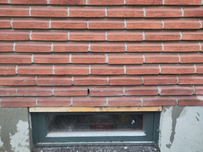 Tegelvägg ovan ett fönster med sprucken rad av tegelstenar, troligen orsakat av armering.