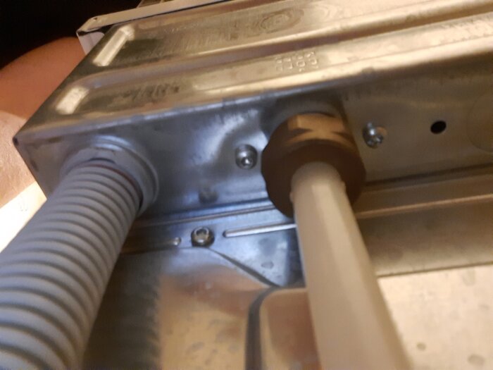 Närbild på baksidan av en maskin där två slangar är anslutna med metallfästen, tagen snett underifrån.