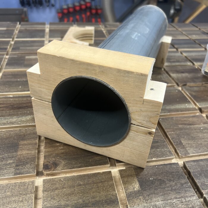 Träfäste monterat på rör, skapat med regel och trallskruvar, ligger på arbetsbänk. Fokus på hålet utskuret för att passa röret.
