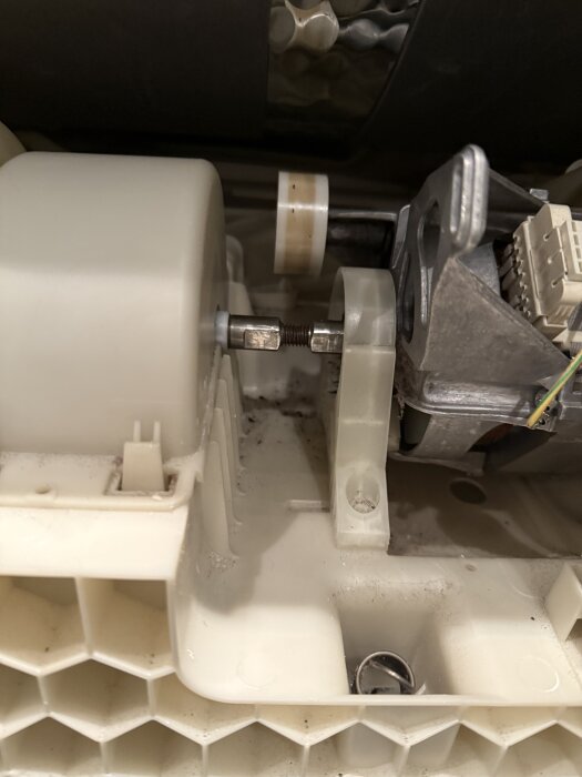 Närbild av insidan av en Bosch kondenstumlare med en vit plastkomponent och synliga metalldelar och kablar, relaterade till drivremmen.