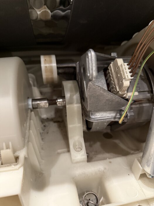 Närbild av insidan av en Bosch kondenstumlare med fokus på drivaxeln och vita plastdetaljer, omgiven av kablar och andra komponenter.