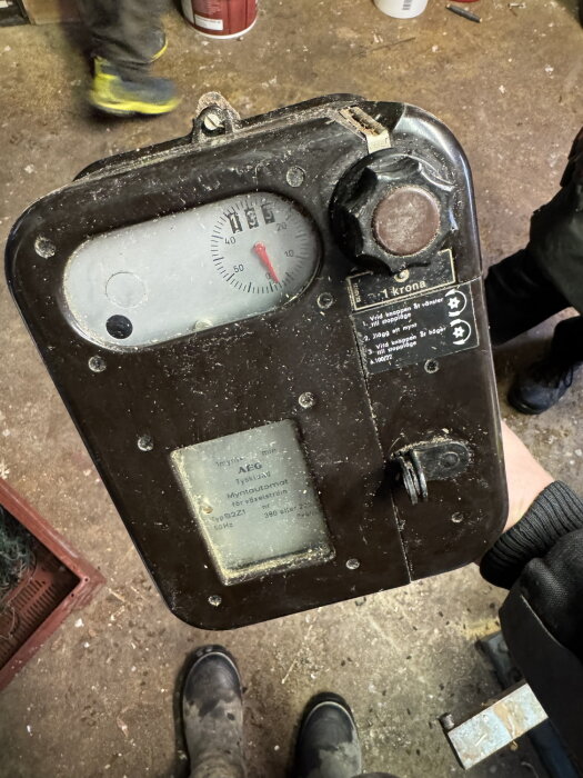 Gammal myntautomat för elektricitet, märkt "AEG" och "1 krona", hittad medan den städas. Den har en urtavla och ett vred, troligen för mobilladdning.