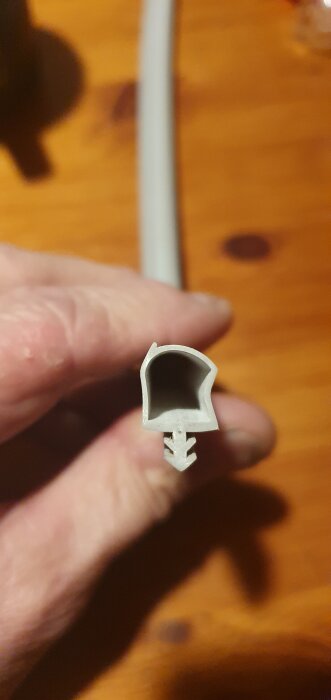 Profilbild av en grå, mjuk gummilist från BTB med pilformad undersida för tätning av ytterdörrar.