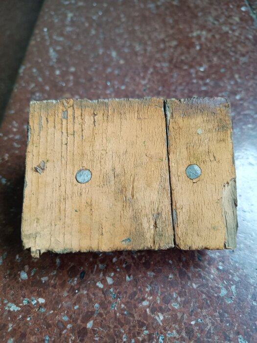 Gammal träbit med två spikar, tecken på slitage och sprickor, del av ett takprojekt med byggfel och problem.