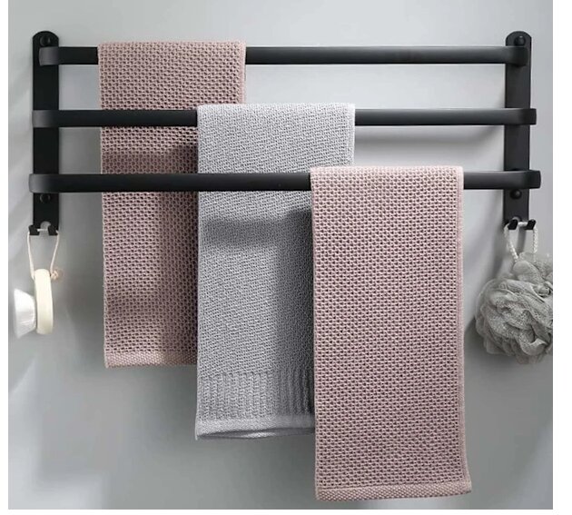 Svart väggmonterad handdukshängare med tre stänger, olika nivåer, med rosa och grå handdukar. Hängare monterad på ljus vägg.