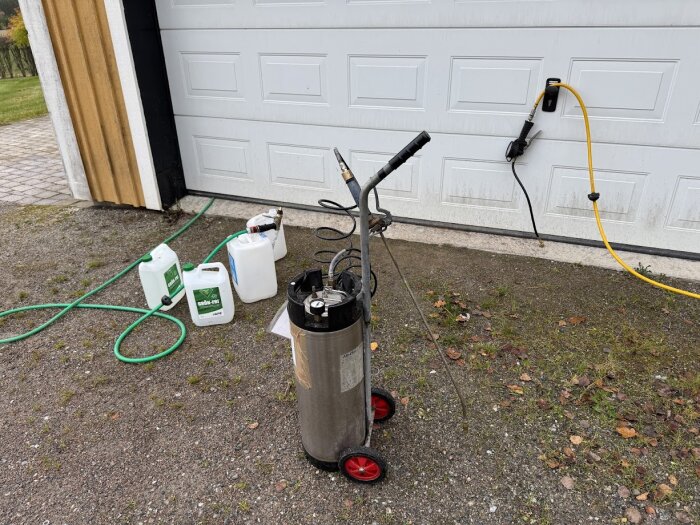 Utomhus vid ett garage med trädgårdsslangar, en trycktvätt och rengöringsmedel för underhållsarbete.