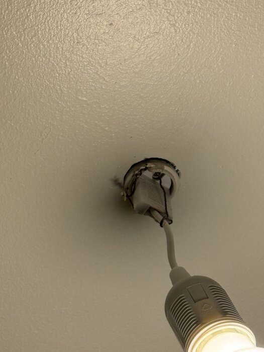 Lampa hänger från taket, upphängd med hjälp av fastighetsskötare, exponerade kablar synliga.