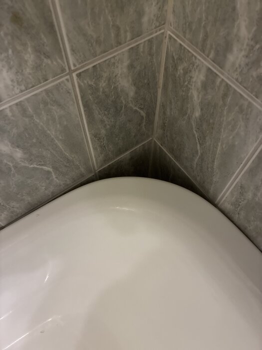 Fristående badkar placerat mot hörn i ett kaklat badrum, synligt utrymme mellan badkaret och väggen där vatten kan rinna ner.