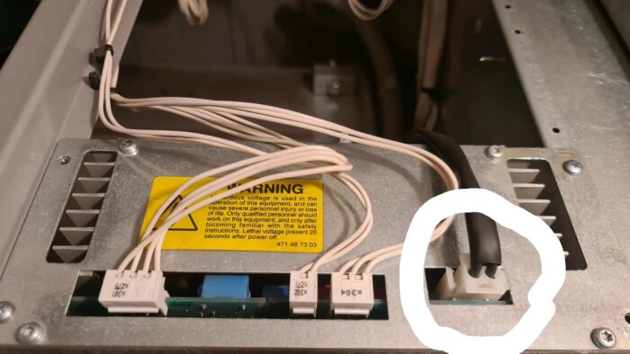 Elkontakt markerad med en cirkel inuti en apparat med flera sladdar och en varningsskylt om spänning.