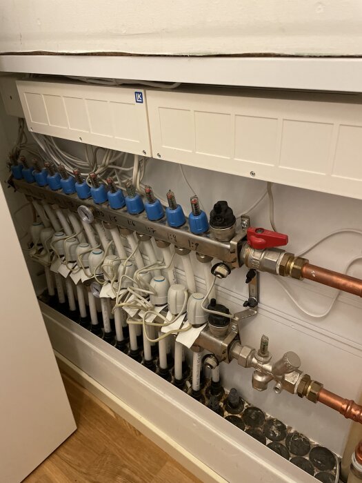 Fördelningsskåp för golvvärme med flera rör och kontroller under installation i ett hus.