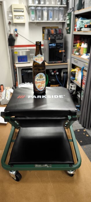 Flaska med öl står på en Parkside arbetsbänk i ett organiserat verkstadsutrymme med hyllor och verktyg.