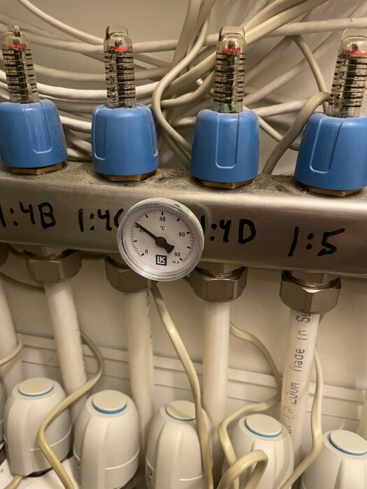 Blå rörkopplingar med mätare och ställdon, markerade med 1:4B-1:5, i ett system, omgivna av flera kablar och en termometer.