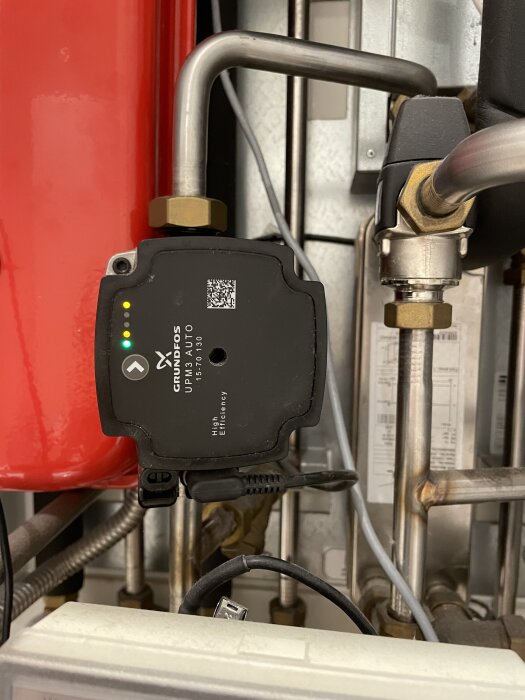 En ställdon installerad på rör, med märket Grundfos synligt på fronten, omgiven av flera rör och anslutningar i en bygginstallation.