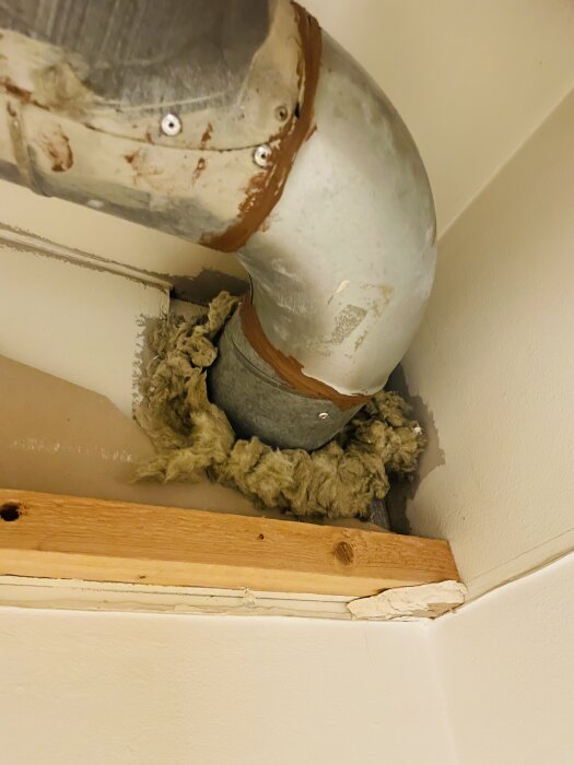 Dammig isolering runt en metallventilation i ett hus, delvis täckt med fogmassa och omgiven av trä och vägg.