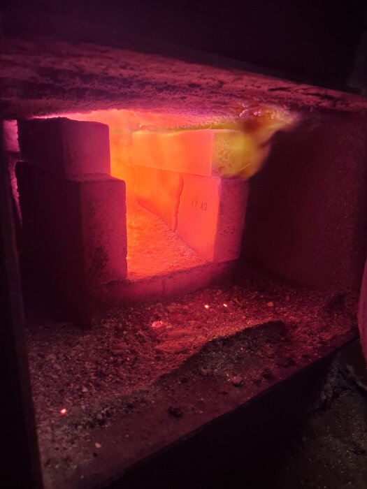 Glödande eld i kamin med packade tegelstenar, sprider värme och ljus i mörk omgivning, relaterar till inlägg om energieffektiv eldning.