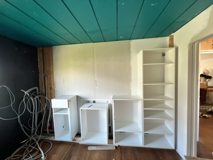 Vita köksskåp mot en nyligen fixad vägg och snirklande kablar till vänster; taket är turkost.