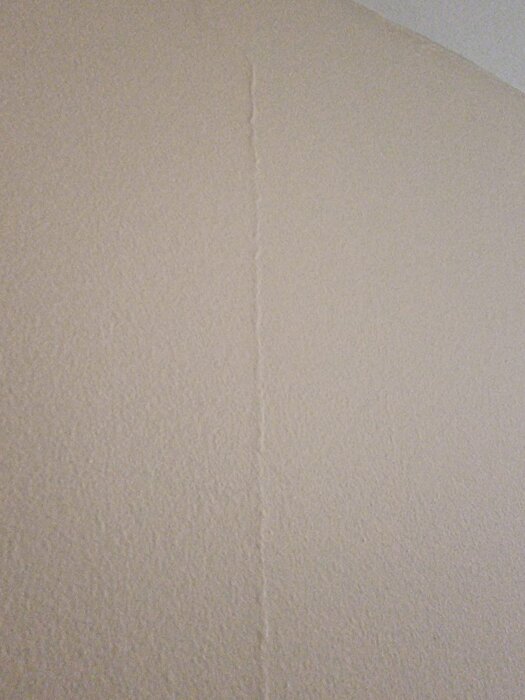 Vägg med vertikal sprickbildning i färgen, antydan till ojämnheter.