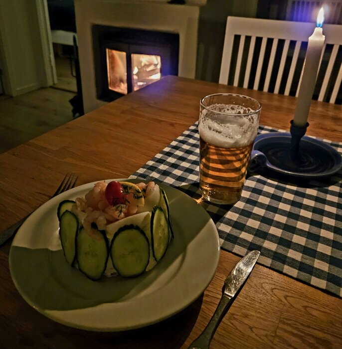 Kvällsmys med öl och räksmörgås på tallrik framför brinnande kamin och tända ljus.