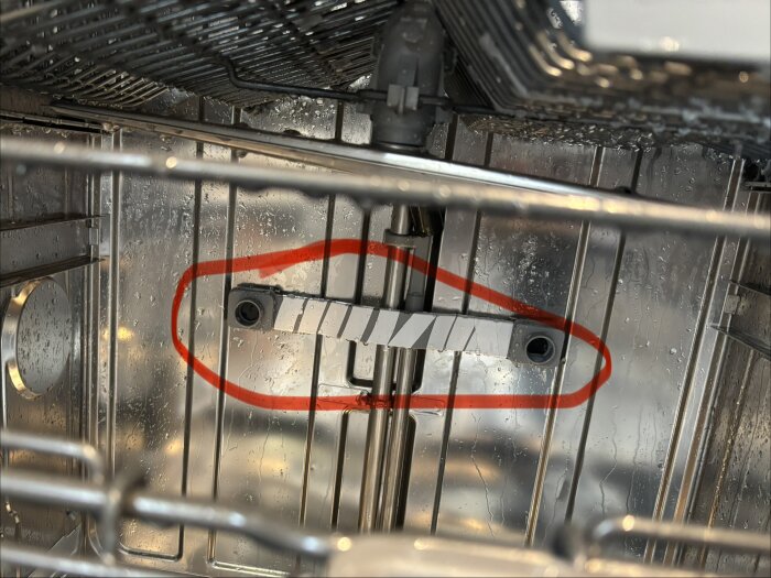 Diskmaskinens inredning med fördelarrör inringat i rött, tydligt sprutat vatten nedåt, potentiellt skadat rör som påverkar funktion.