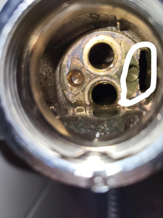 Inuti duschblandaren syns två runda öppningar och en oregelbunden, vitmarkerad form, vilket tyder på potentiell metallförlust.