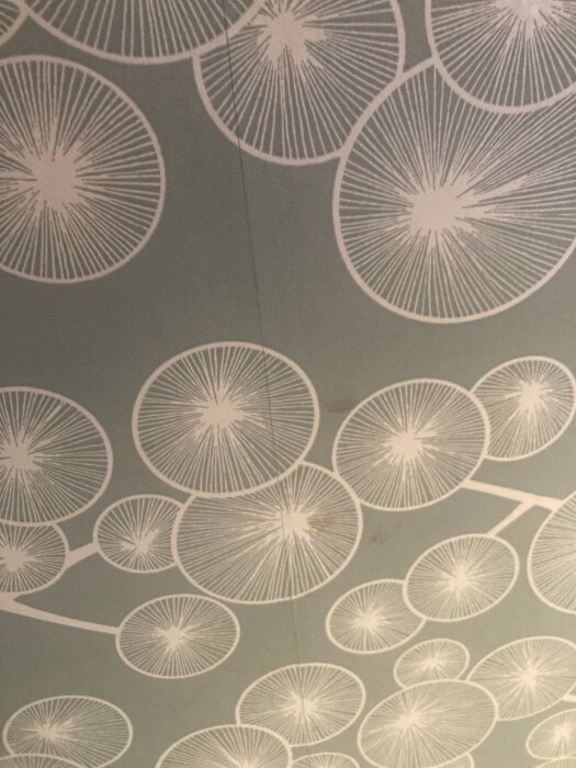 Tapet med cirkulärt mönster i vitt på gröngrå bakgrund, synlig skarv mellan tapetvåderna.