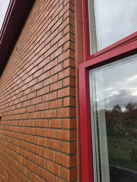 Tegelfasad med fönster, röda fönsterramar och regn på glaset, möjligt projekt för montering av stående panel.