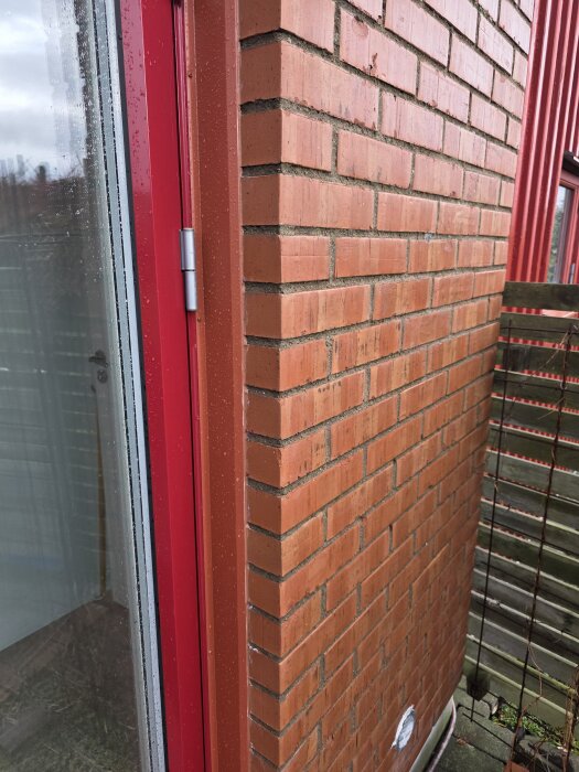 Tegelfasad vid altandörr med röda metallsmygar, visar tegelfog och eventuell fuktproblem vid höstregn.