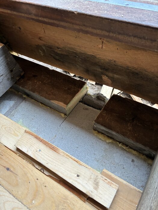 En del av reglar och syll på ett sutteränghus, med synliga fläckar på träet och isolering under, fotograferad inomhus.