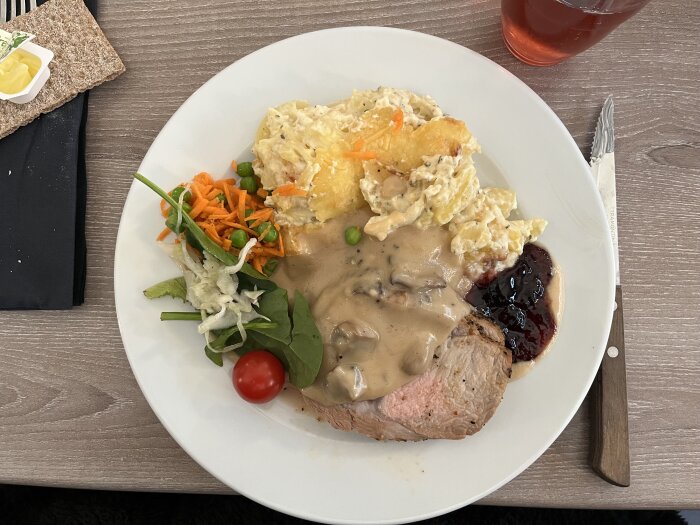 Helstekt entrecote med potatisgratäng, svampsås och gelé på en tallrik, serverad med sallad och en körsbärstomat.