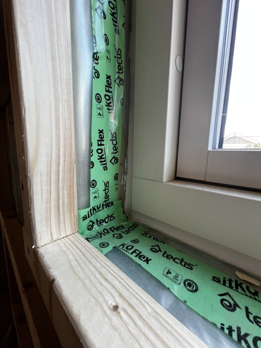Grönt sitkfönstertejp applicerat mellan träkarmen och fönsterkarmen i fönsterhålet, visar plastens placering i monteringen.