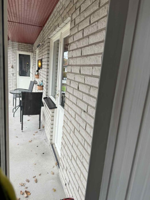 Altandörrar med takutsprång och utemöbler på en stenlagd uteplats.