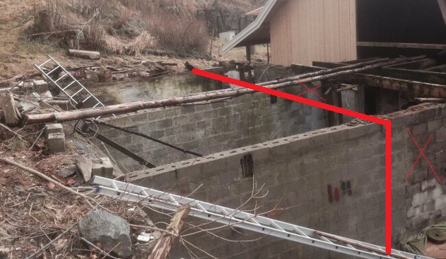 Foto av en gammal betonggrund i en slänt, delvis riven, med röda linjer markerande var ny mur planeras; omgivande lantlig miljö.