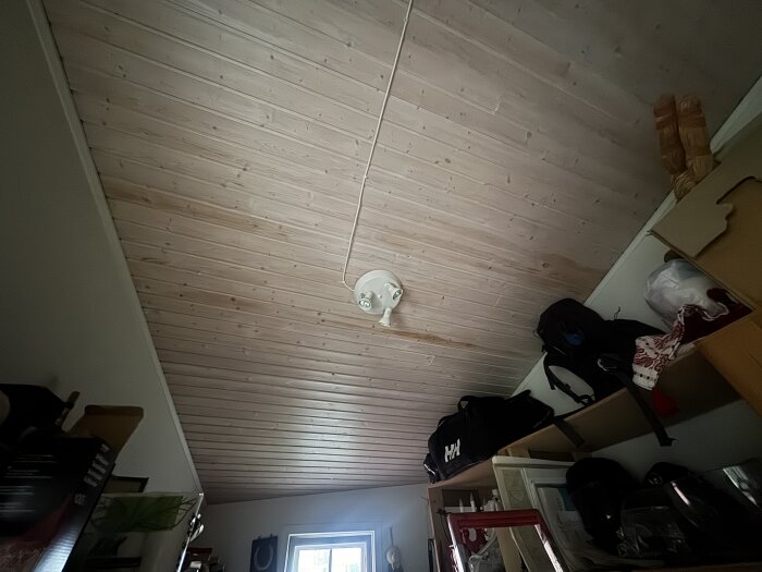 Innertak av trä med mörkare fläckar ovanför hyllor i ett förråd, potentiellt orsakade av fukt.