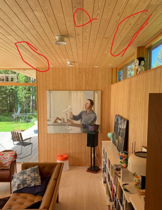 Furupaneltak med skiftningar i färgen markerade med röd penna, inomhusrum med konstverk, bokhylla och utemöbler i bakgrunden.