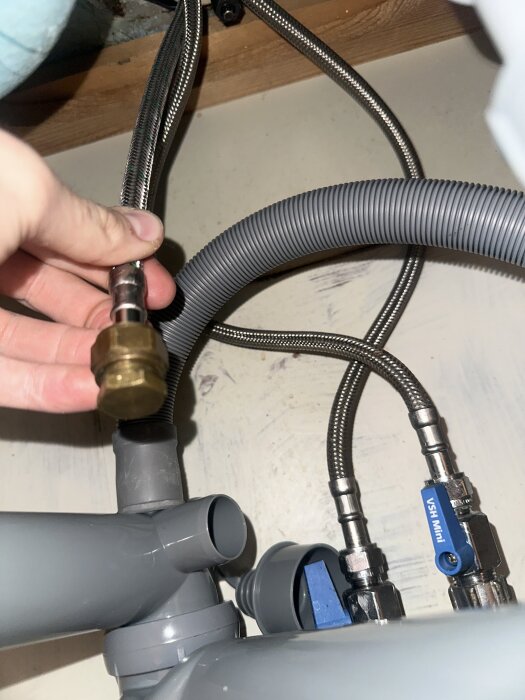 Hand som håller en slang kopplad till en VVS-ventil, med en mässingplugg fastsatt, i ett kök under vasken.