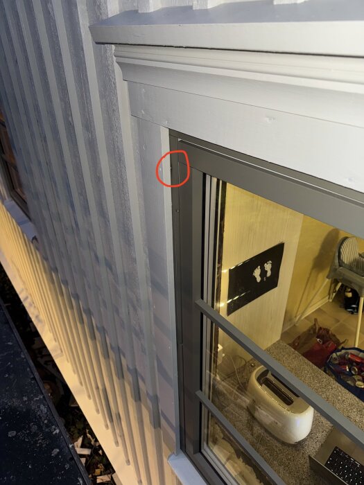 Närbild av ett aluminiumbeklätt fönster från Elitfönster. Foder är spikat på panel och genom aluminium, markerat med röd cirkel.