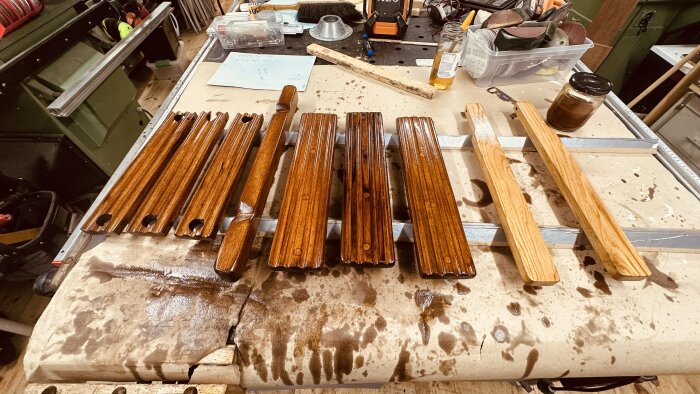 Mörka och ljusa träbitar ligger på ett arbetsbord, täckta med utspädd Benar, i en verkstadsmiljö med verktyg och material i bakgrunden.