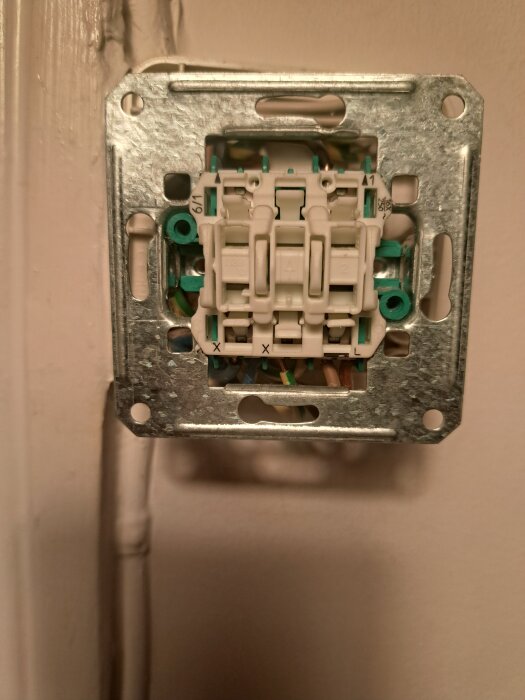 Vägguttag med synliga kablar, kopplingsbox och fästram för elinstallation.