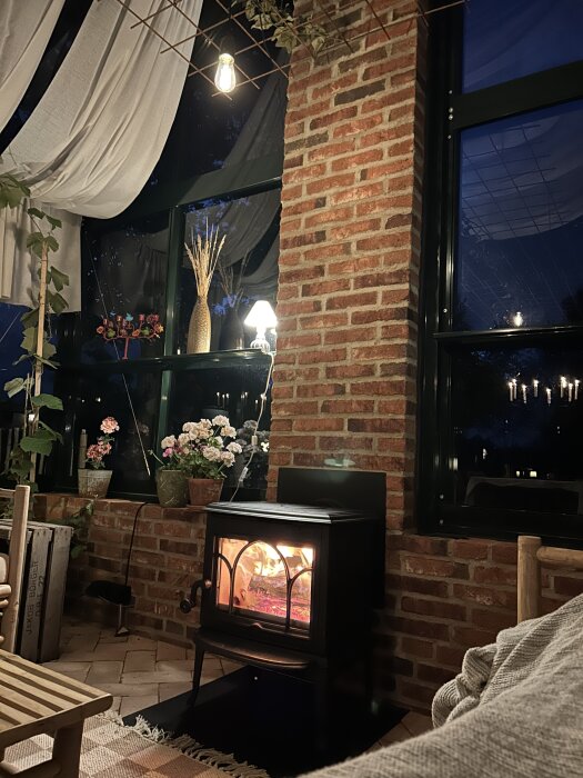 Mysigt växthus interiör med tegelvägg, eld i braskamin och blommor i fönsterbrädan.